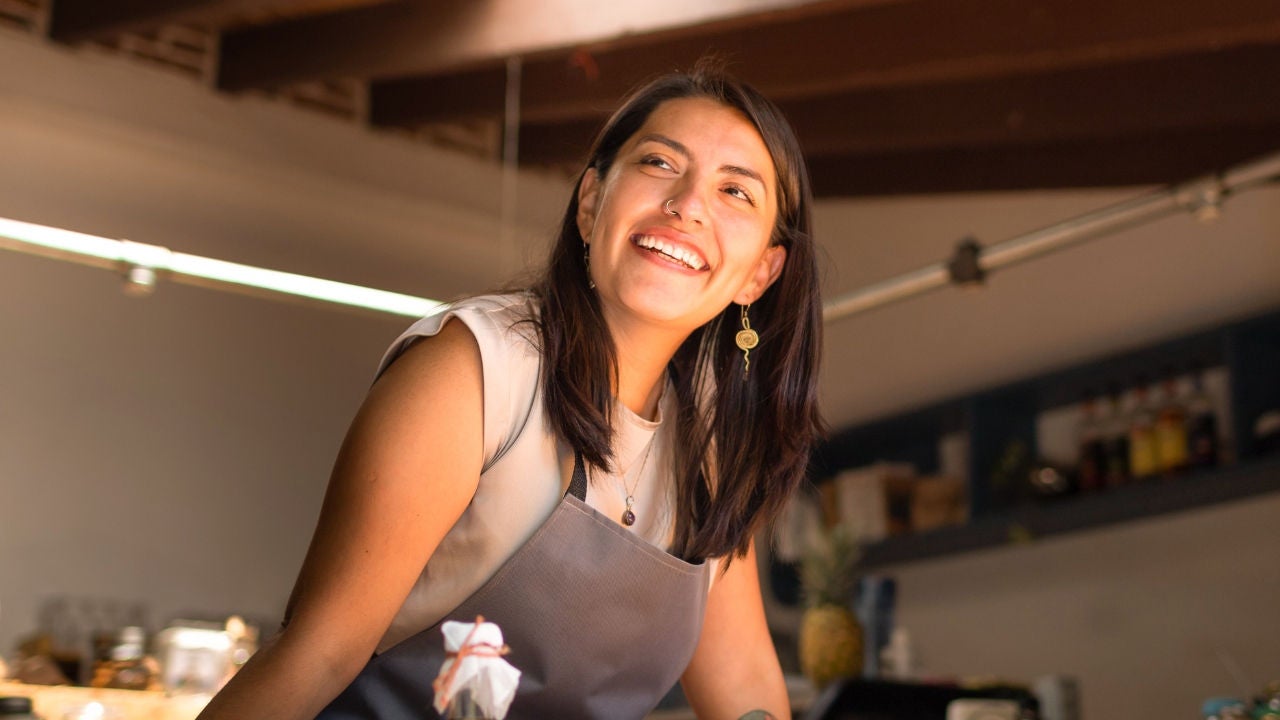A woman in an apron leans over a counter in a store that is just opening. 