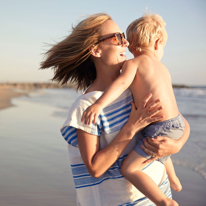 En kvinde holder et barn på en strand.