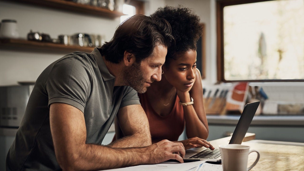 A couple look at their laptop in their kitchen.