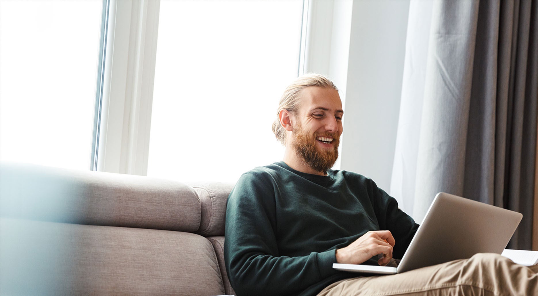 Man smiling while using his laptop on the sofa