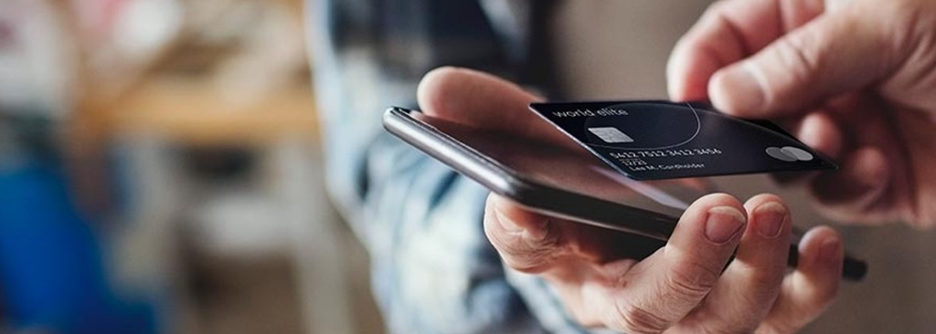 Nahaufnahme von Händen, die ein Smartphone und eine Kreditkarte benutzen, was auf eine Online-Zahlung hindeutet. 
