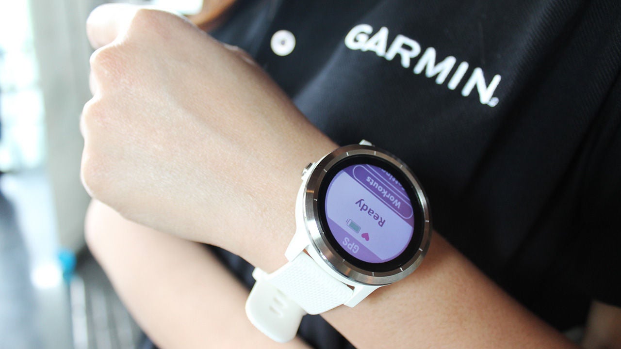 Garmin okosóra viselése közben érintéses fizetésre kész képernyő látható, sportos környezetben, Garmin feliratú pólóval.