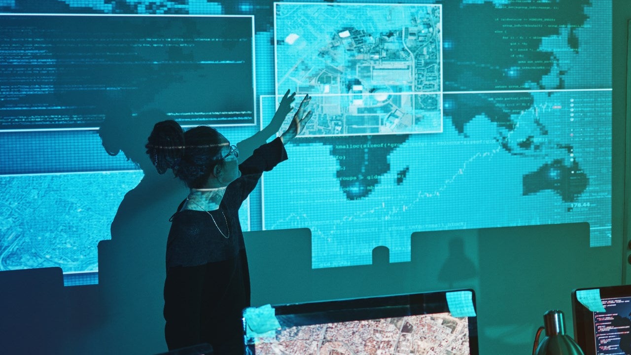 A cyber analyst points to a projected map on a wall. 