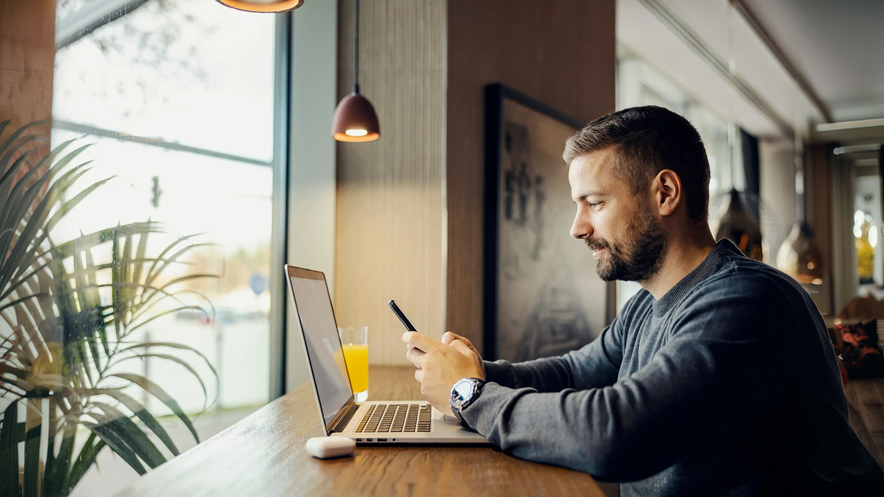 A man sitting at a table using a laptop and phone