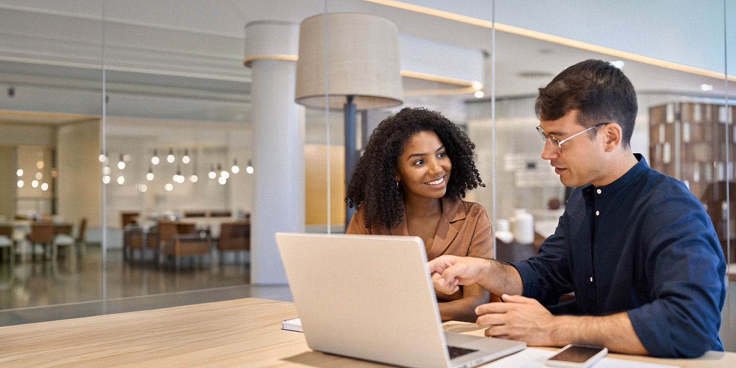 Two coworkers collaborating at the office while using a laptop