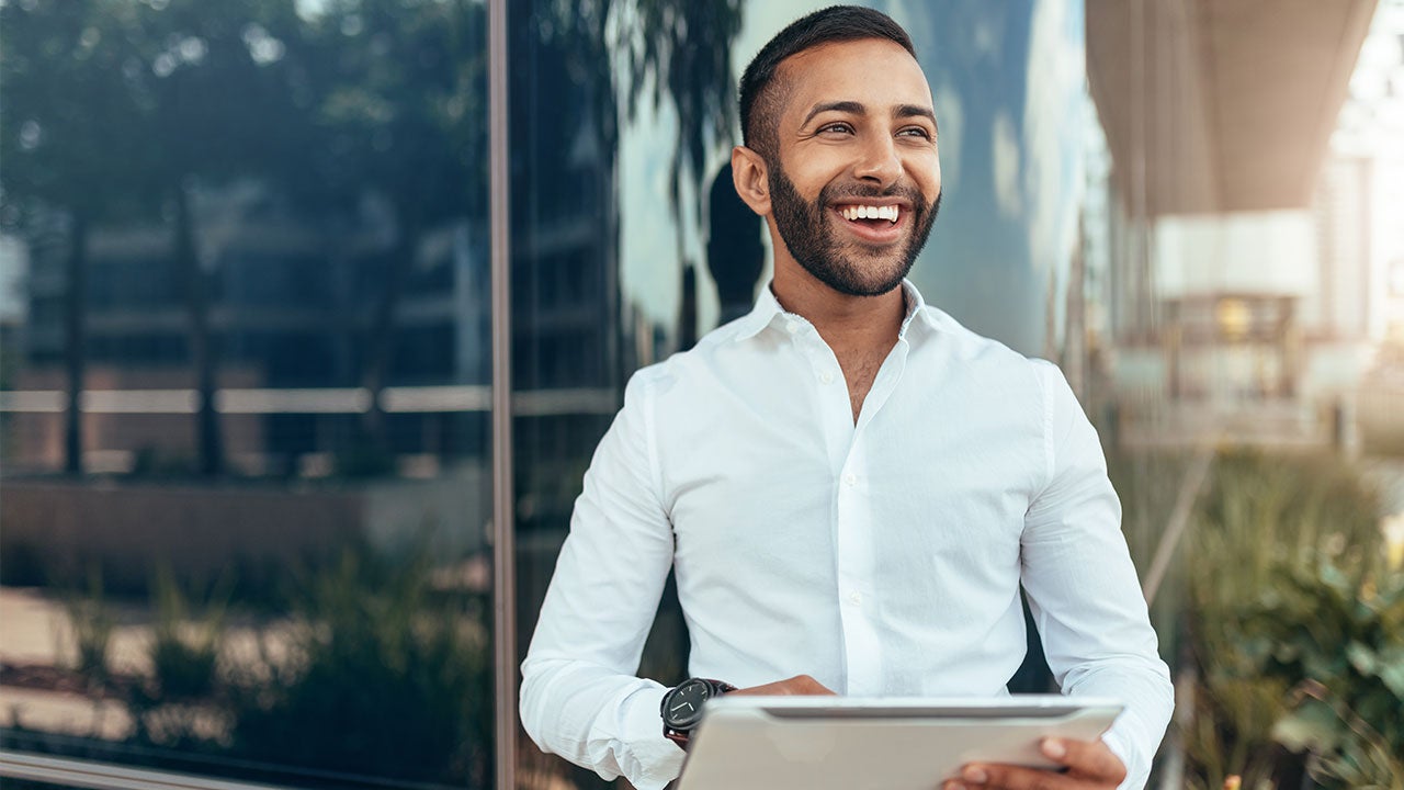 Un homme souriant tenant une tablette et regardant au loin.