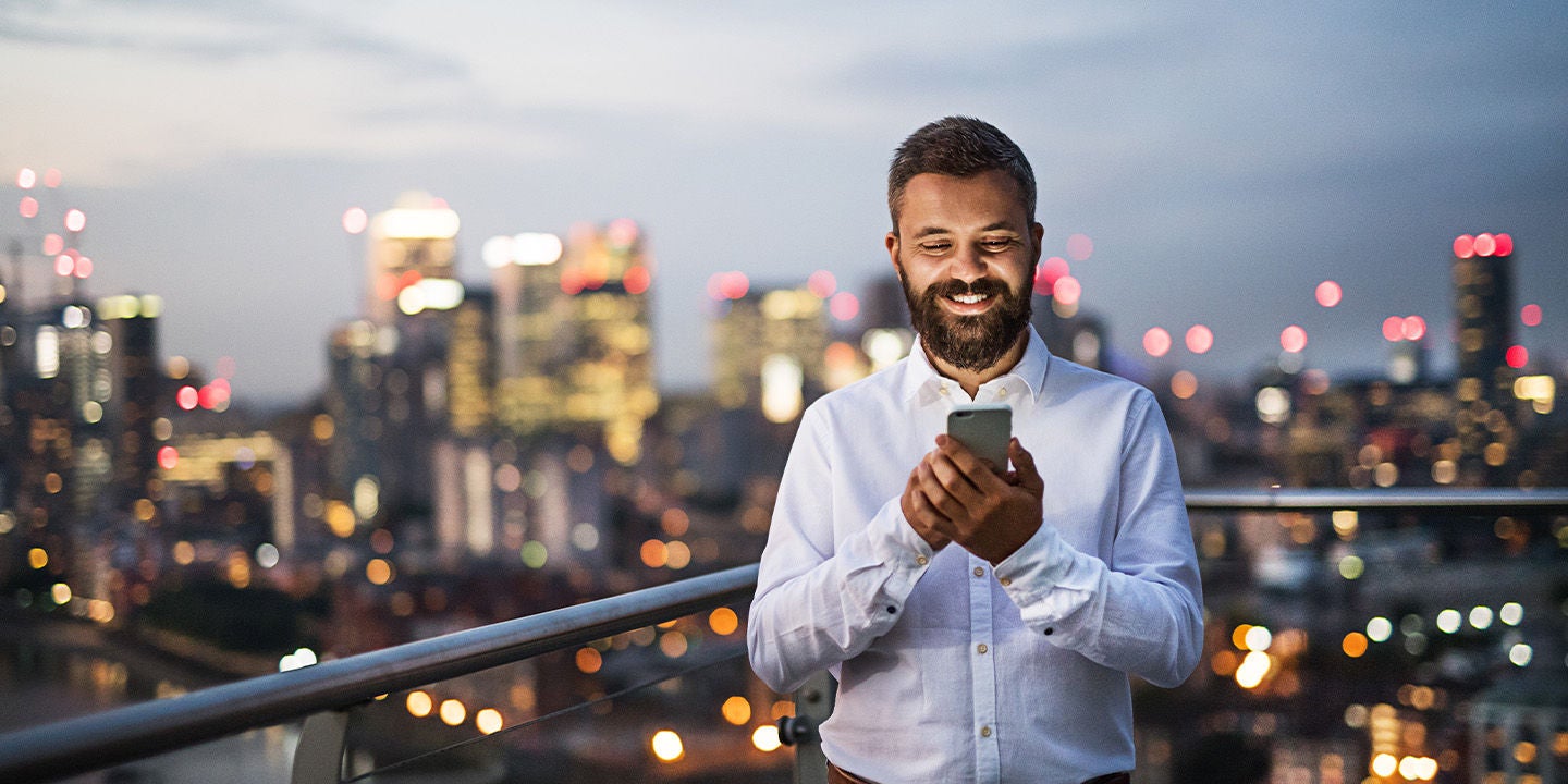 Man smiling while using his phone with city skyline in the background