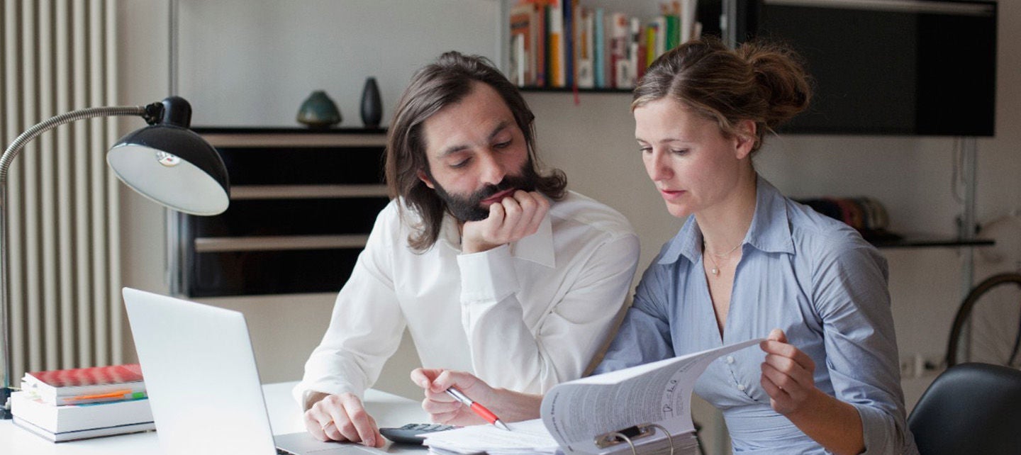 To personer som jobber sammen ved et skrivebord med en bærbar datamaskin og papirer.