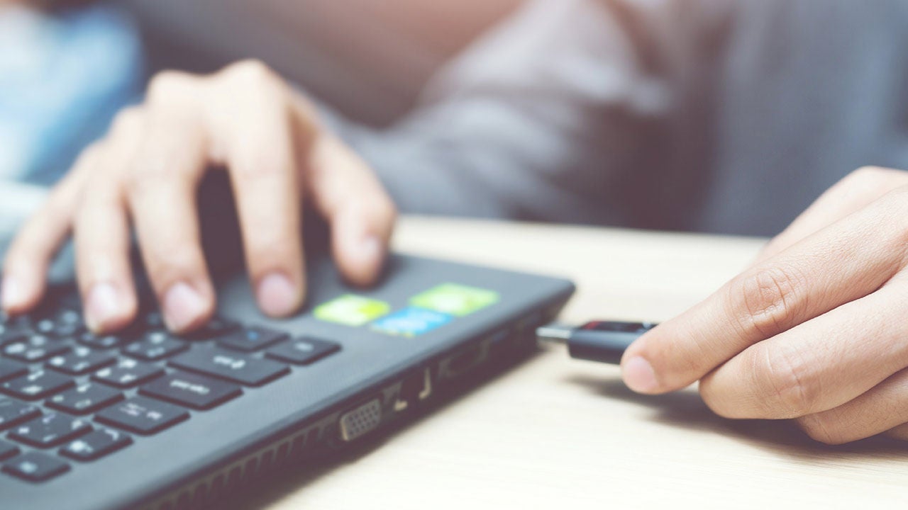 Close up of male hand plugging pen drive on laptop at home.
