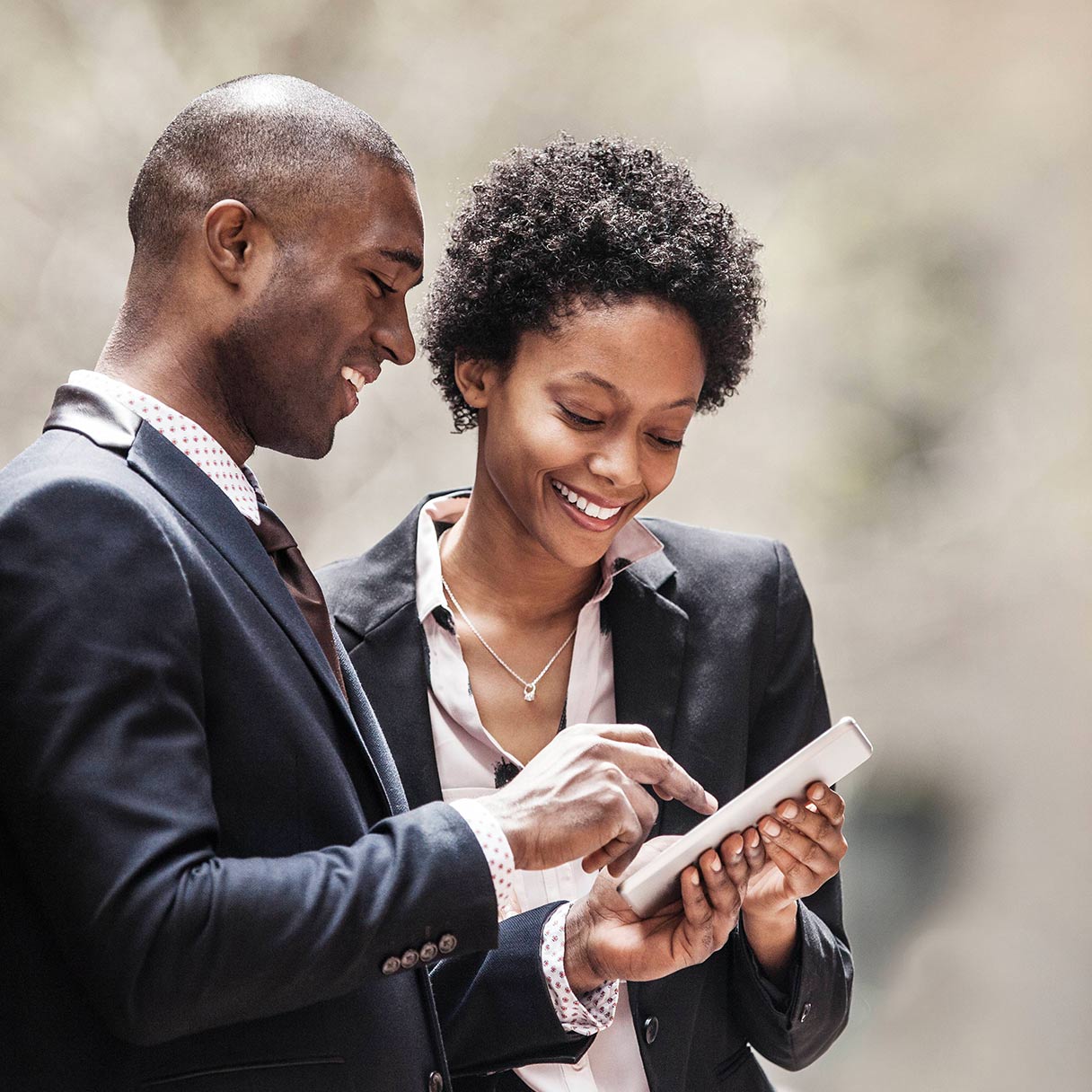 Two coworkers smiling while looking at a tablet together.