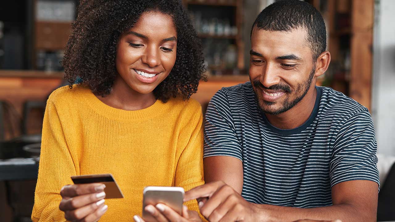 Two friends looking at phones while using credit card