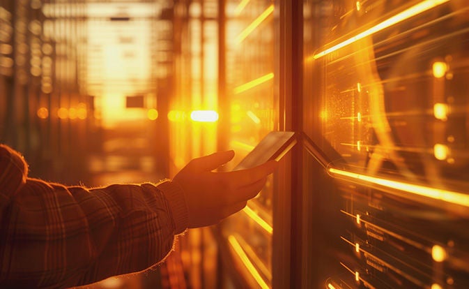 A worker holds a tablet device against a data center unit. 