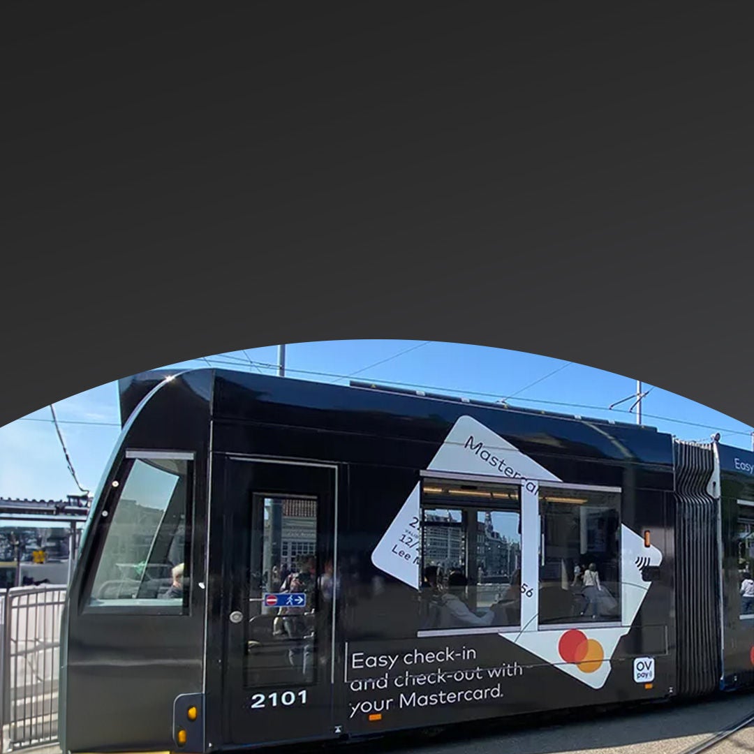 Black tram with Mastercard urban mobility advertisement on it sitting at a station.