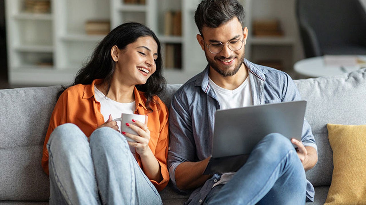 Två personer sitter på en soffa och tittar på en mobiltelefon.
