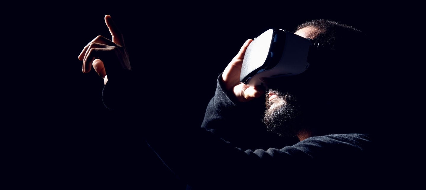 A man wearing VR googles holds up his hand as if touching something with one finger. 