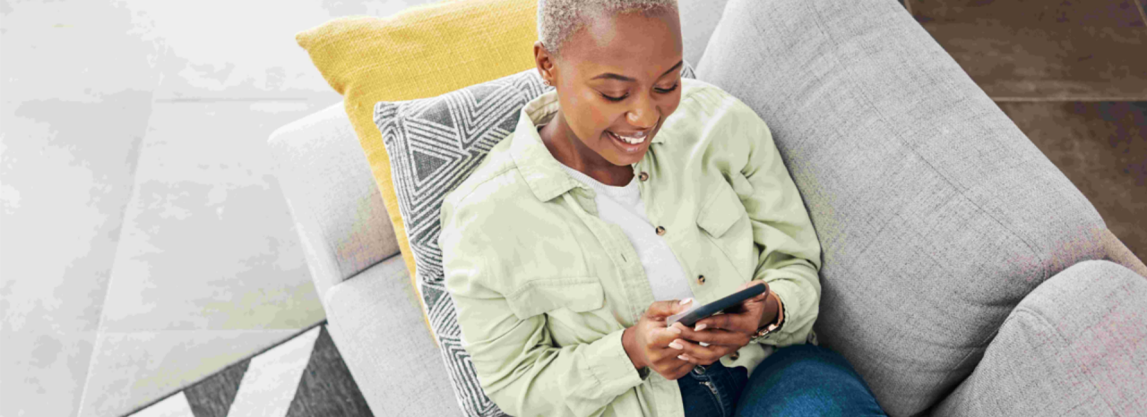 A woman sits on a couch looking at her smartphone