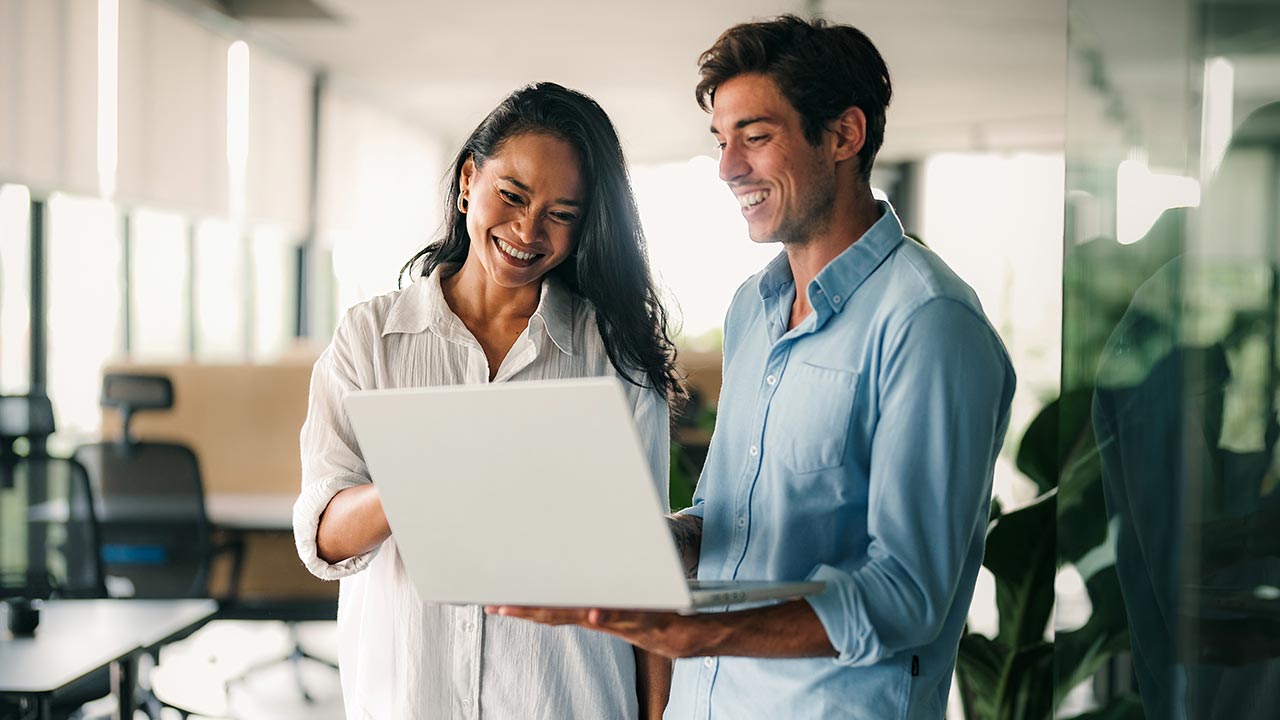 Two colleagues standing to review laptop.