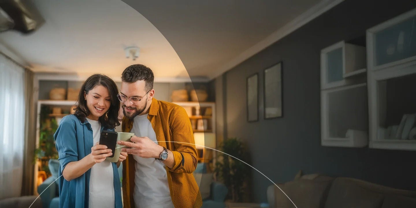 בעל ואישה מאושרים שותים כוס קפה בזמן שהם משתמשים בטלפון נייד.