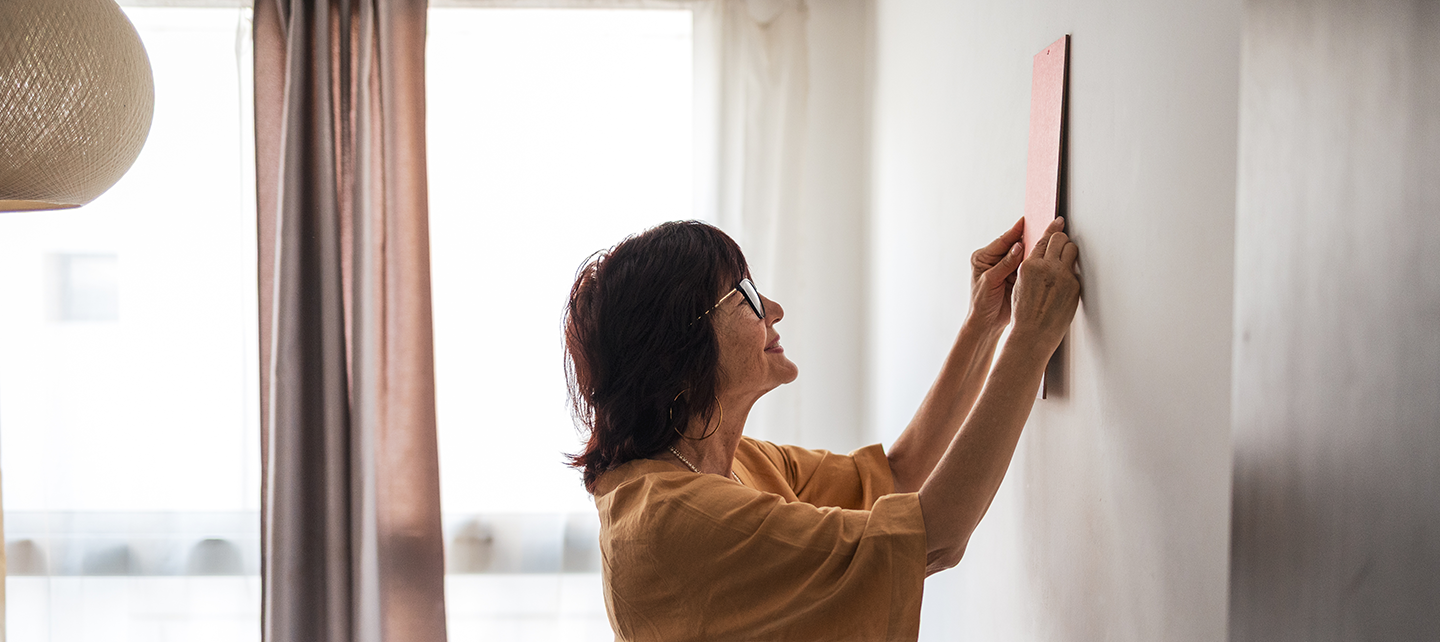 Older woman putting up art in her home