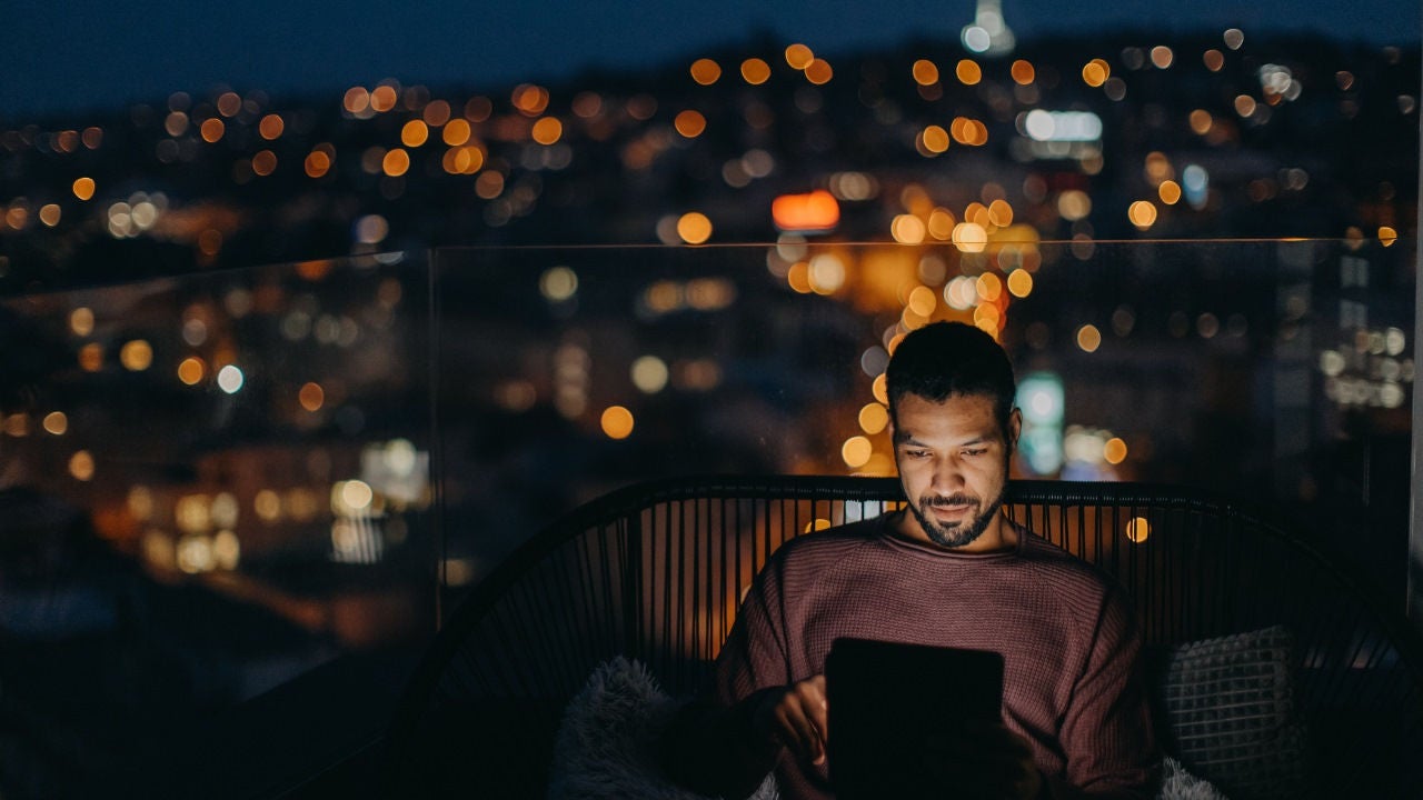 A man looks at his tablet on a balcony at night. 