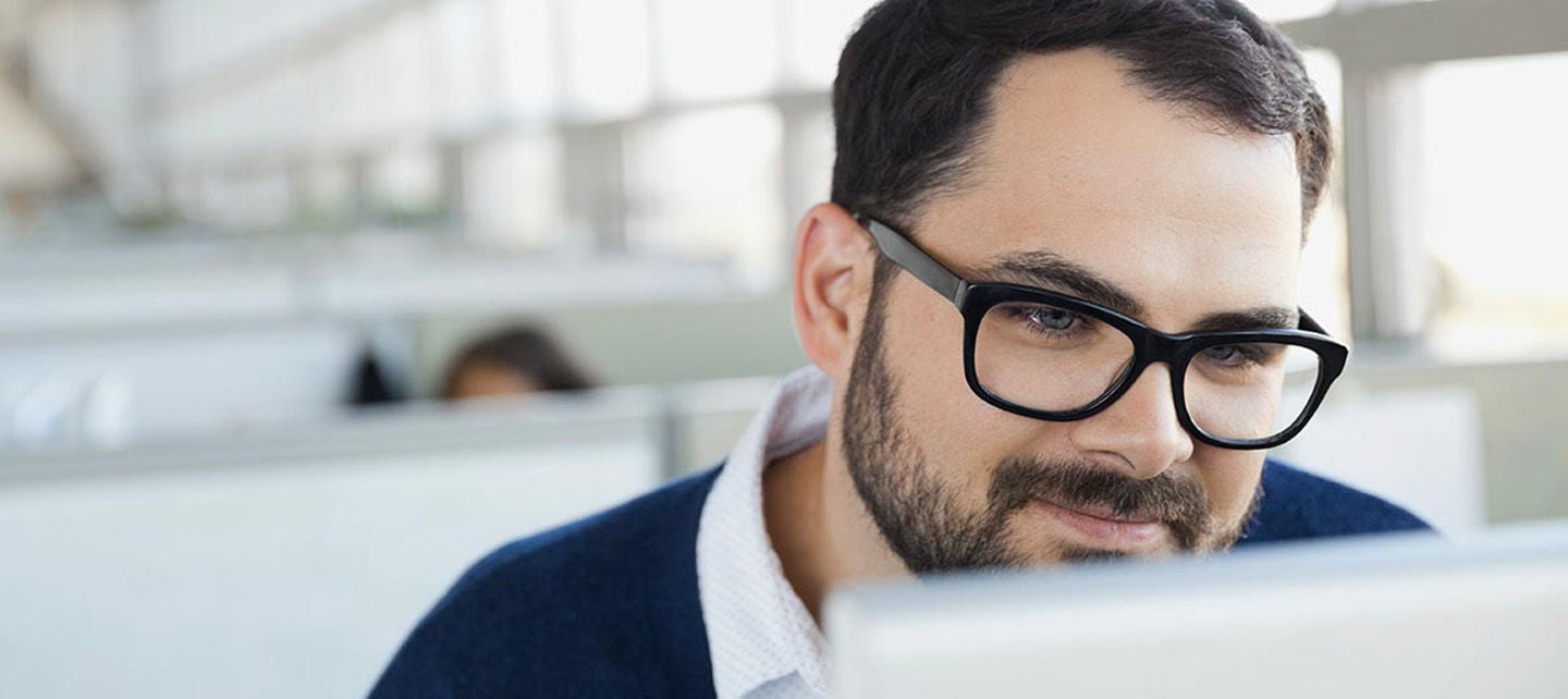 Nært bilde av mann iført briller fokusert stirrer inn i PC skjermen.