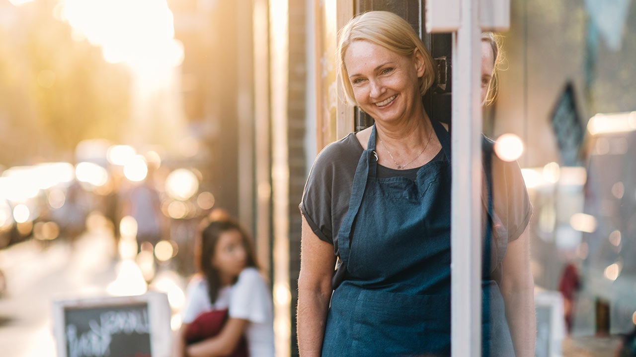Confident female owner standing at entrance of deli.