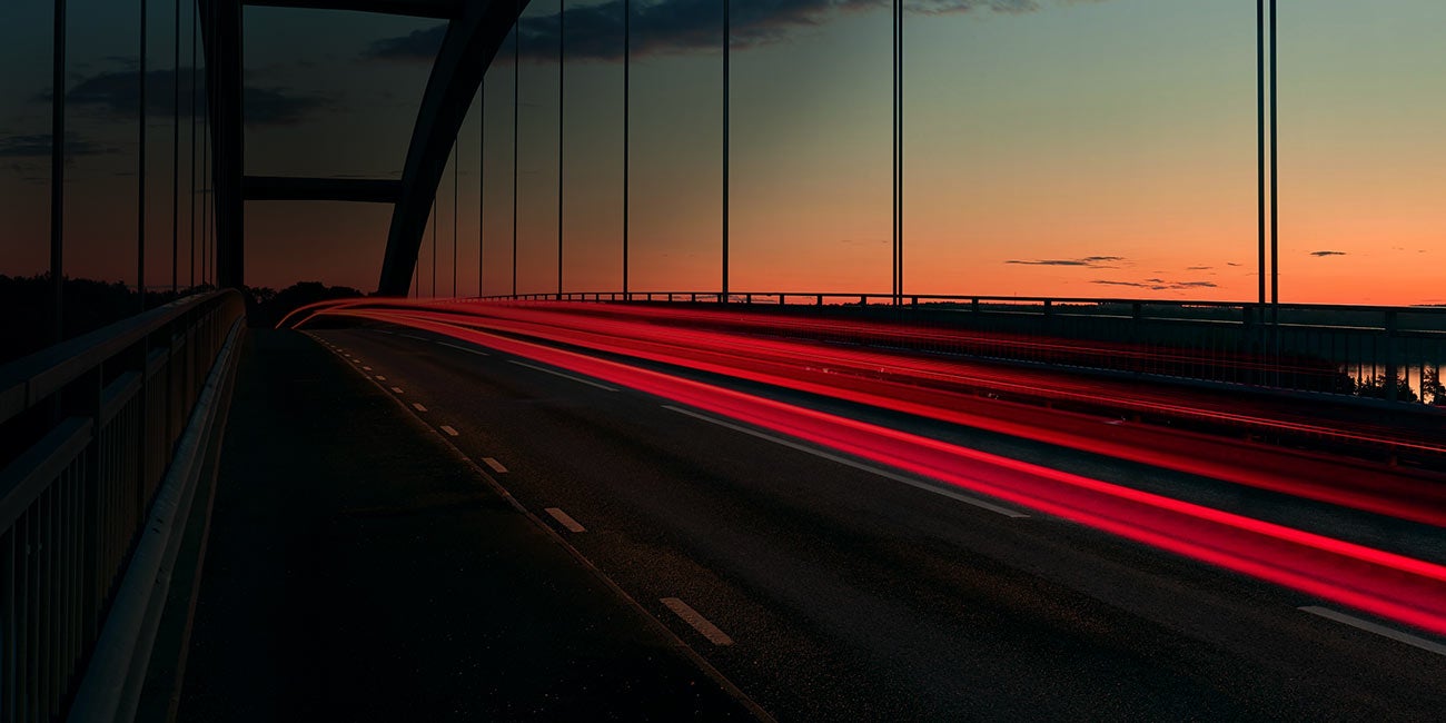 Híd naplementében, piros fénycsíkokkal az elhaladó járművektől.
