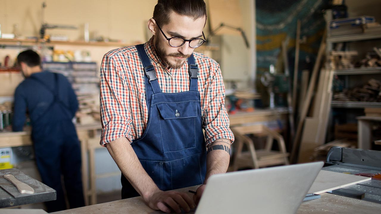 Craftsman using laptop in woodworking shop.