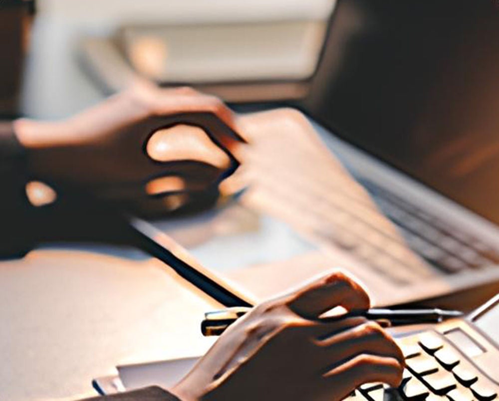A person working at their desk using a calculator and laptop.