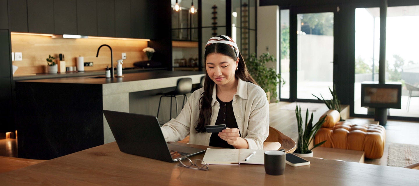 Woman at a kitchen table, shopping on her laptop