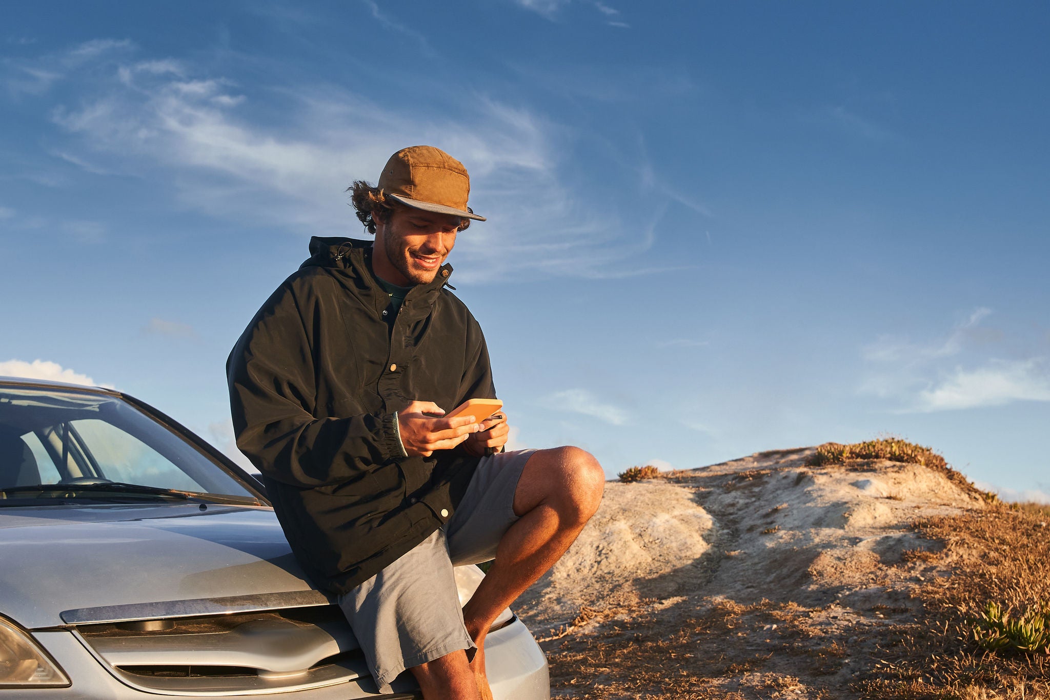 Čovjek gleda u svoj telefon dok sjedi na automobilu u prirodi.