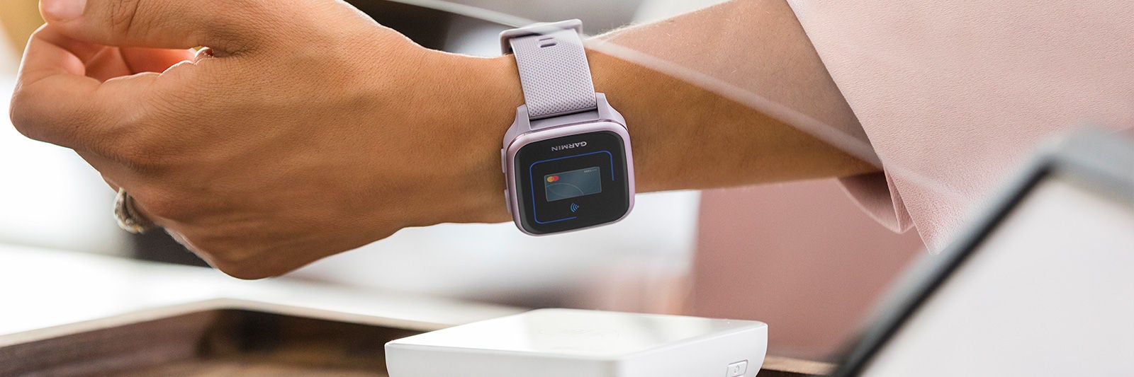Garmin okosórával végzett érintéses fizetés közelről, bankkártya-terminál felett, világos és modern környezetben.