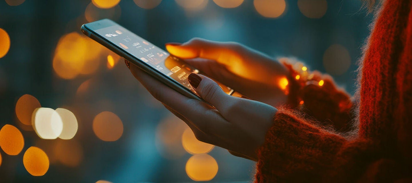 A woman's hand holding the phone against a dark background with multi-colored lights. 