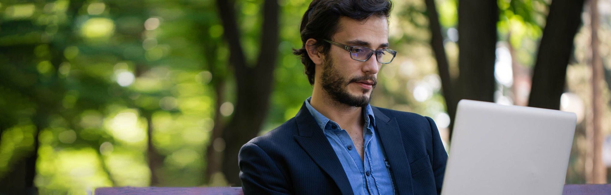 Homem de terno e gravata em um parque olhando para um laptop