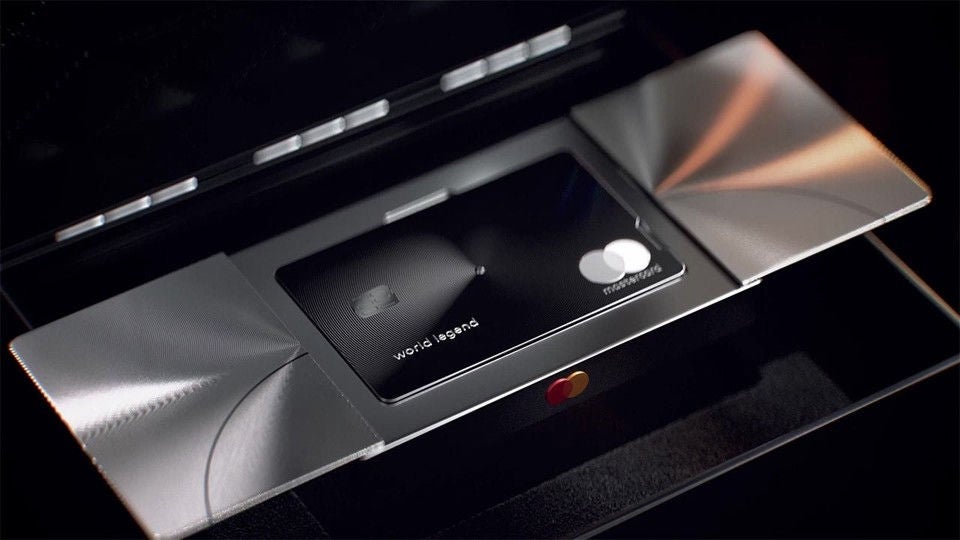 A black metal payment card printed with the words world legend rests in a glass display case under dark lighting.