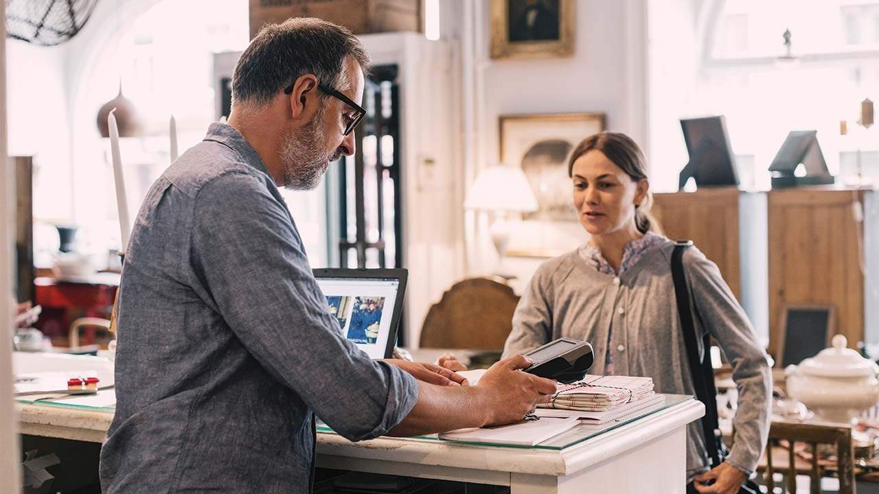 Egy vásárló bankkártyával fizet egy üzlet pultjánál, miközben az eladó terminált tart a kezében.