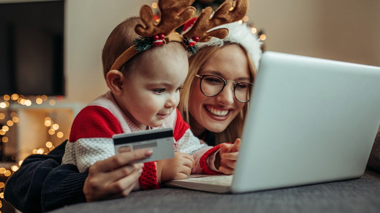 A woman in a Santa hat and a young girl in an antler headband look at a laptop while the woman holds a credit card. 