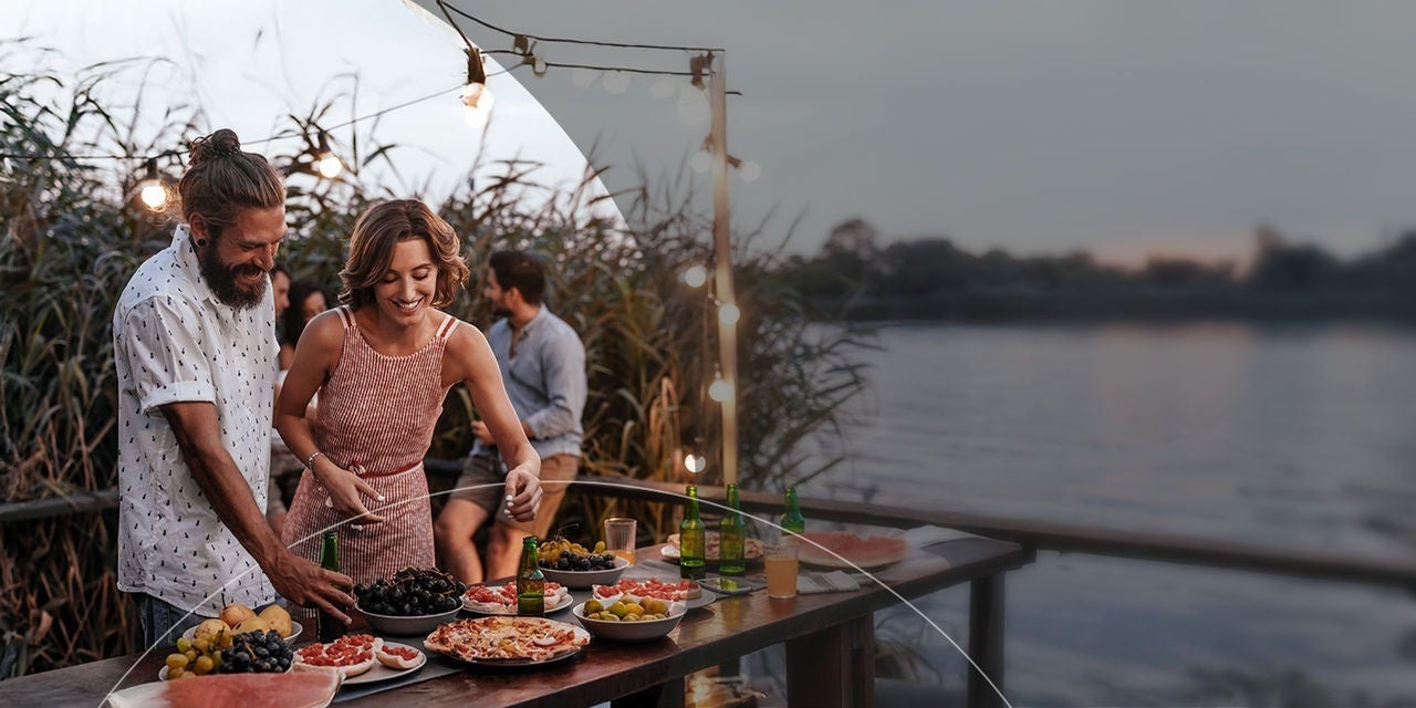 זוג מחייך ליד שולחן על שפת האגם עם אוכל, נהנה ממפגש שמח עם חברים.