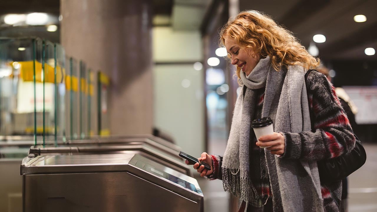 Woman checking out at subway station, using mobile phone.