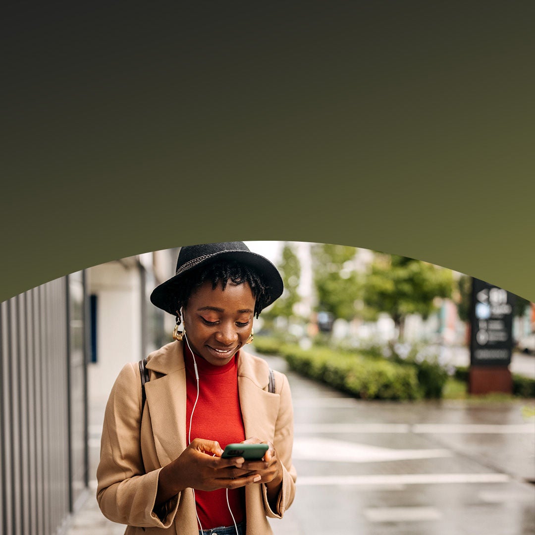 woman wearing a hat walking with phone in hand.