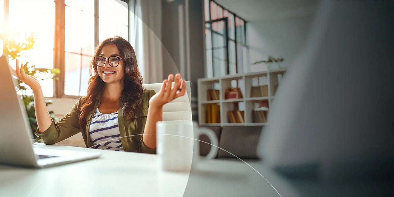 אישה יושבת ליד שולחן כתיבה, ידיה מורמות, מביטה במחשב הנייד שלה, מביעה התרגשות או הפתעה.