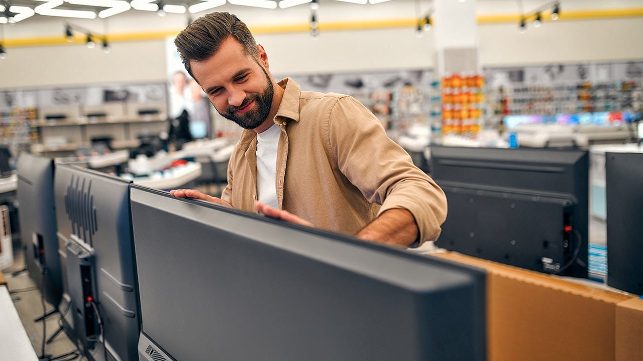 A man excitedly shopping for TVs in large store.