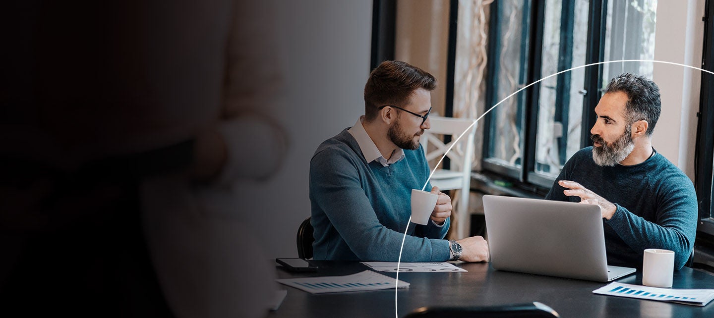 Kolege sjede za stolom i razgovaraju.