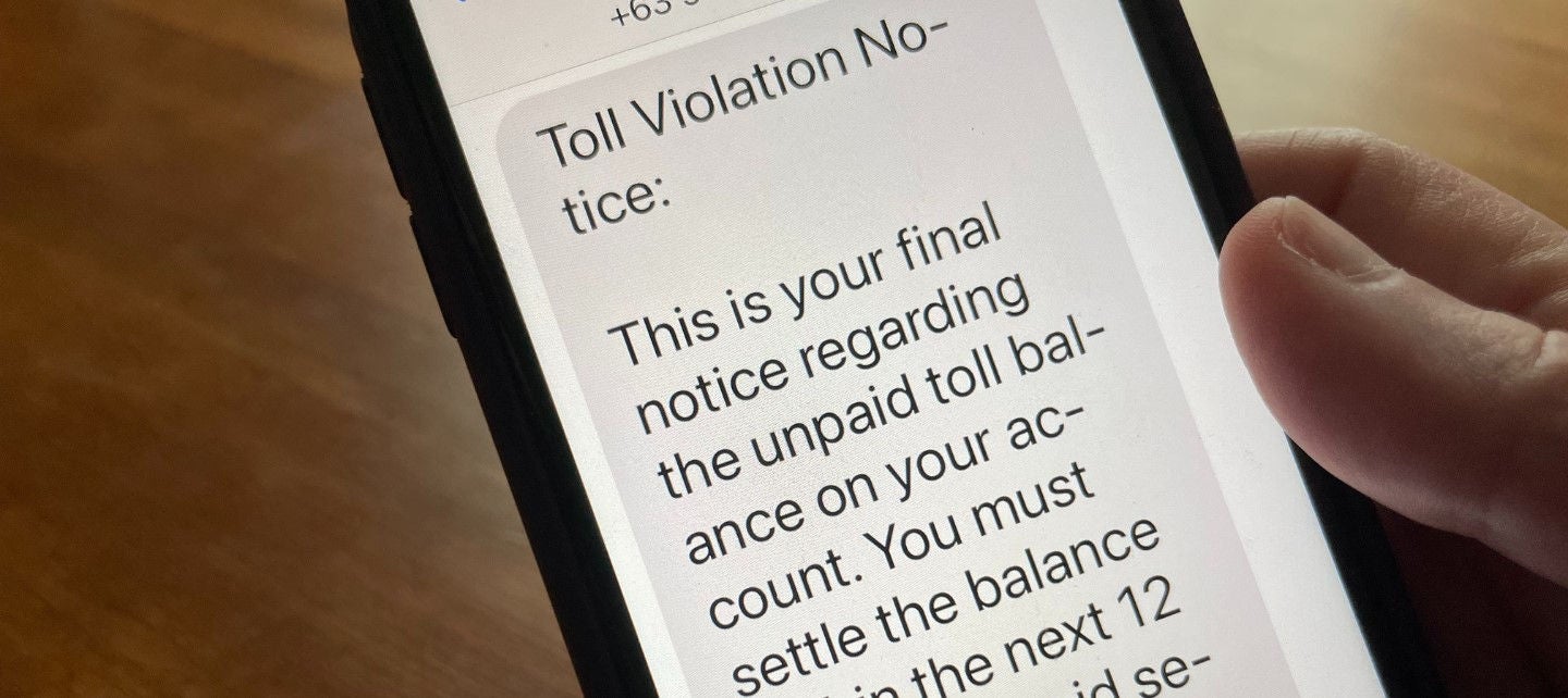 A person holds a cell phone with a text scam notification on it about a toll violation.