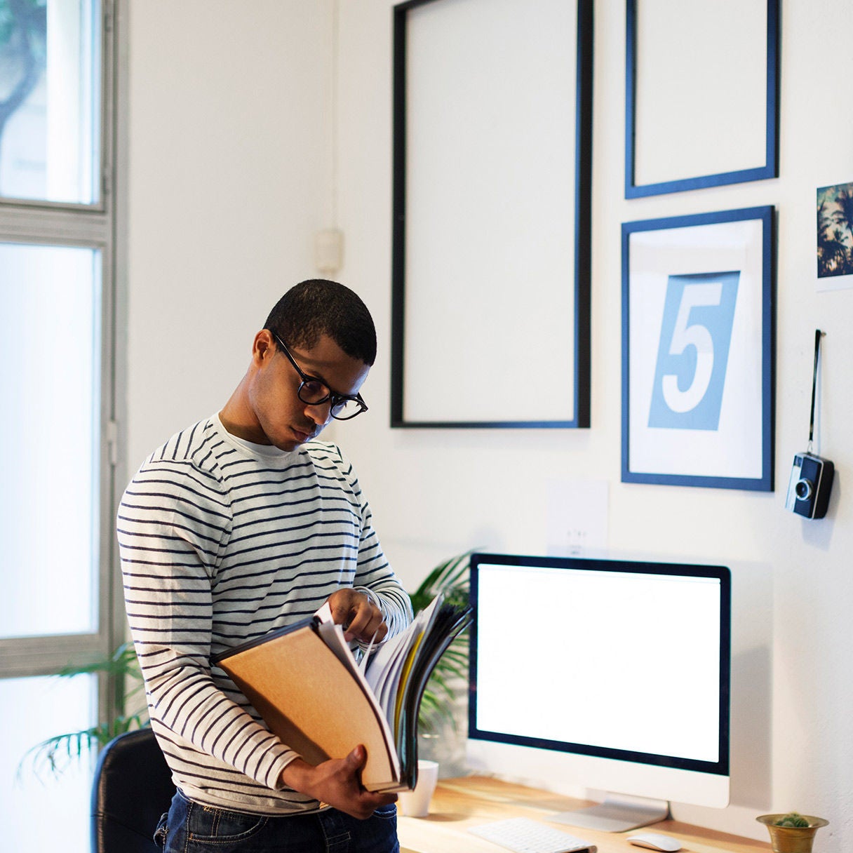 Man holding folders in an office beside a desk and computer monitor.