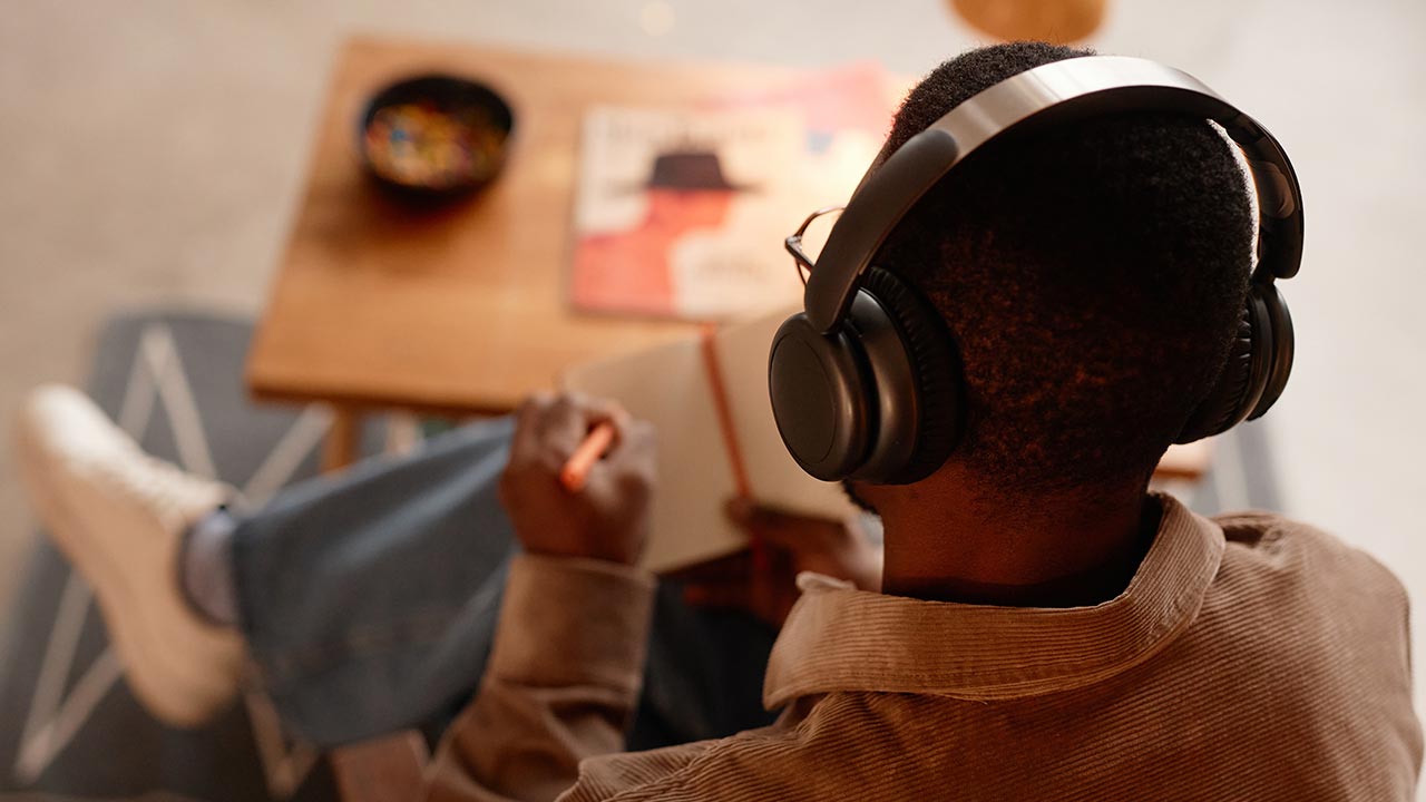 Back view of man with headphones taking notes.