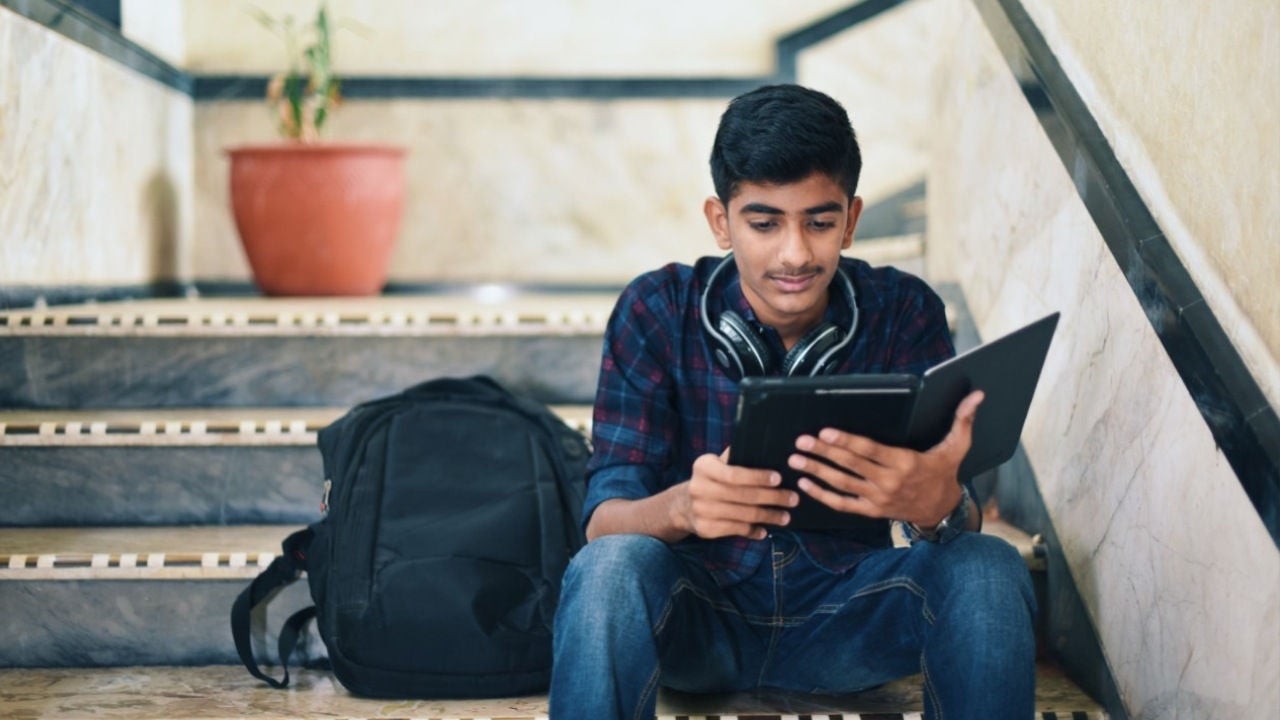 A teenager sits on steps looking at a tablet. 