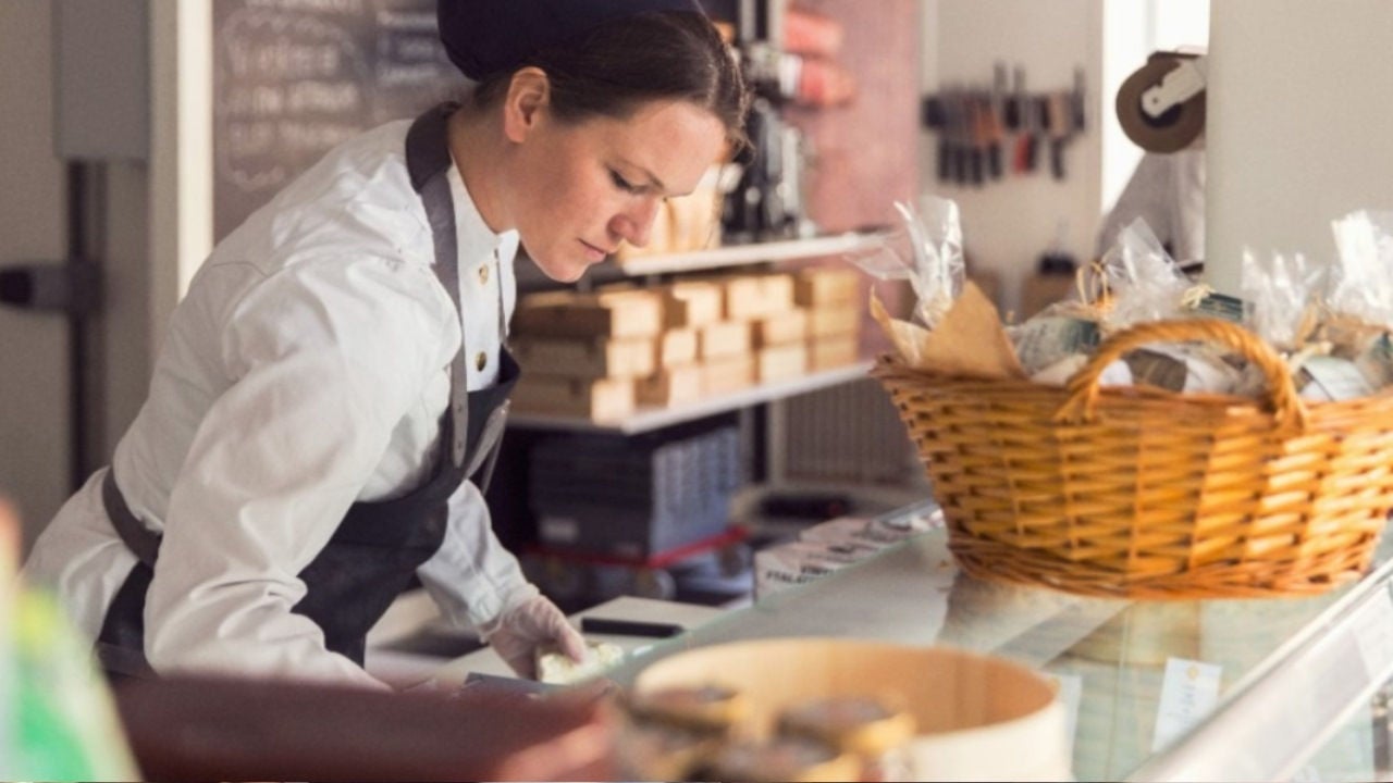 A woman in an apron does paperwork on a counter in a store. 