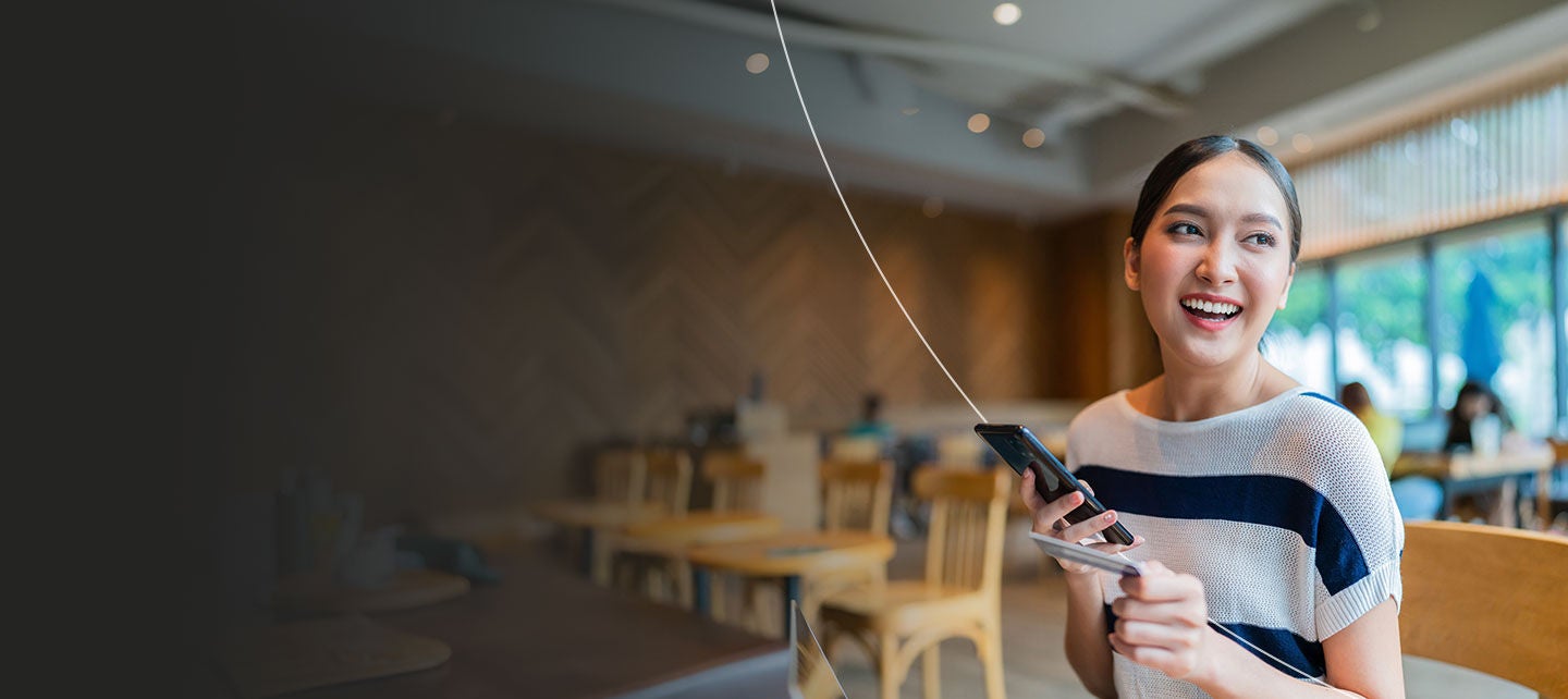 Women holding phone in one hand and payment card in the other hand.