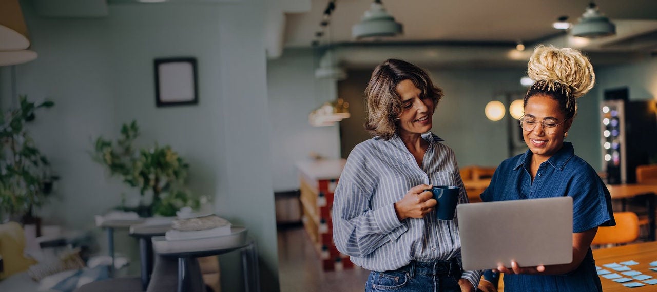Two women standing in a room with a laptop